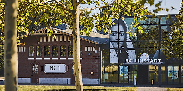 Backsteingebäude des Auswanderermuseums BallinStadt mit Glasfassade und Porträtmotiven, grüne Wiese im Vordergrund