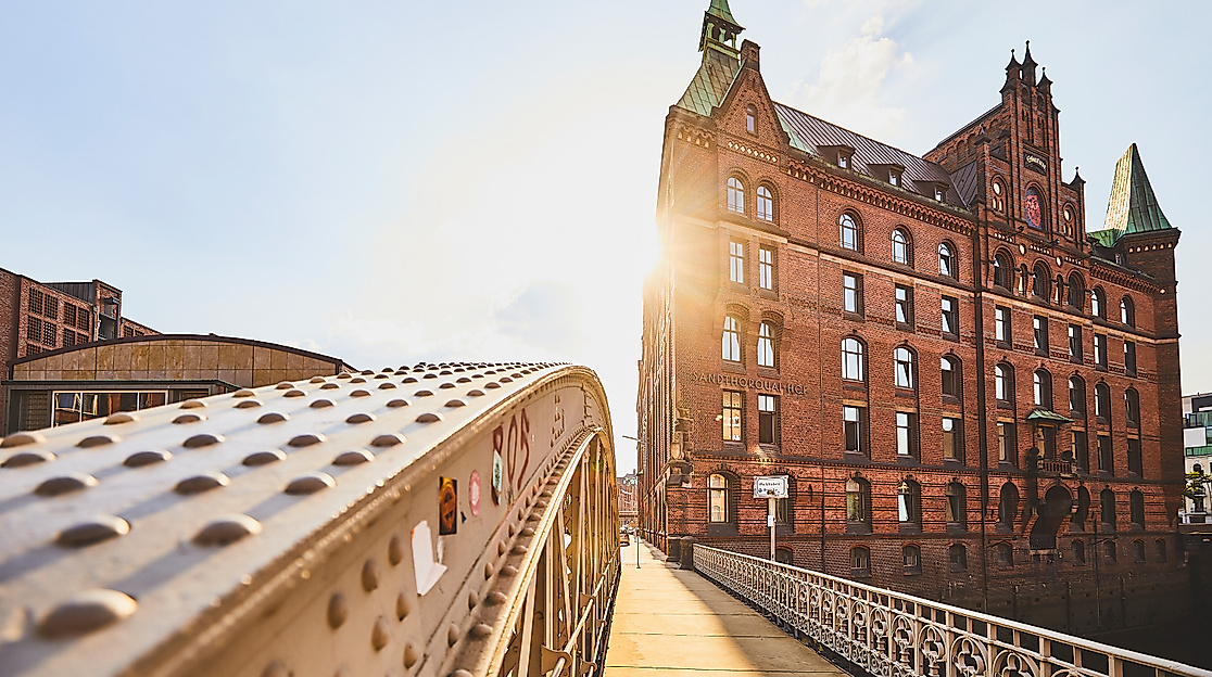 Sonnenlicht fällt auf eine Stahlbrücke am Sandtorkai mit Blick auf ein historisches Backsteingebäude der Speicherstadt