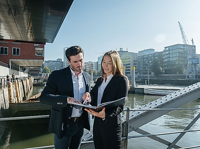 Zwei Geschäftsleute im Gespräch mit Tablet in der Hamburger HafenCity bei sonnigem Wetter
