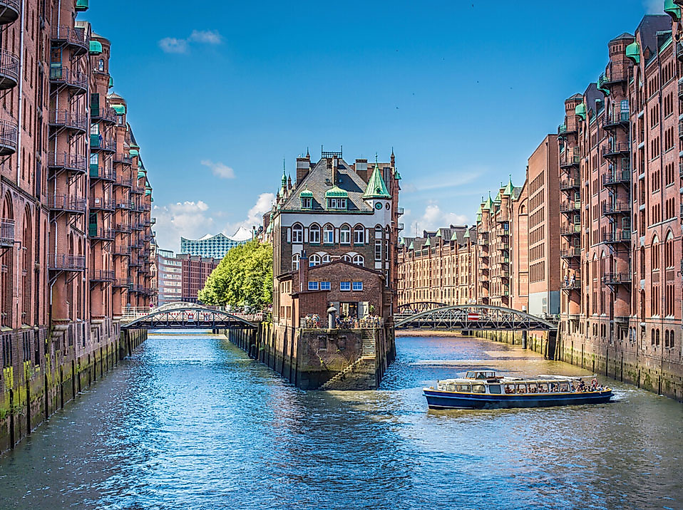 Das Wasserschloss in der Hamburger Speicherstadt zwischen zwei Fleeten bei Sonnenschein, vorn eine Barkasse.
