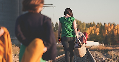 Gruppe junger Menschen spaziert bei Sonnenlicht entlang stillgelegter Bahngleise in ländlicher Umgebung