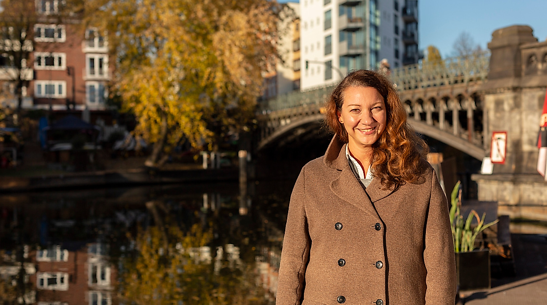 Lächelnde Frau vor Brücke und Kanalufer an der Hamburger Alster bei Sonnenlicht und herbstlicher Stimmung