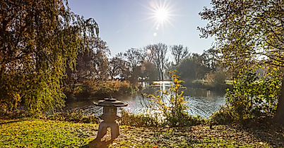 Sonnenlicht über der von Bäumen umrahmten Außenalster in Hamburg mit glitzerndem Wasser und grüner Uferlandschaft