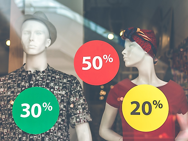 Schaufenster mit Rabattaufklebern in Rot, Gelb und Grün mit 20 %, 30 % und 50 % Sale-Aktionen