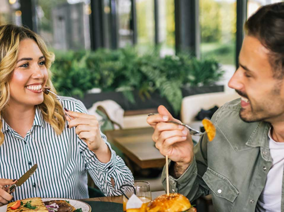 Zwei Männer und eine Frau essen an einem gedeckten Tisch und lachen