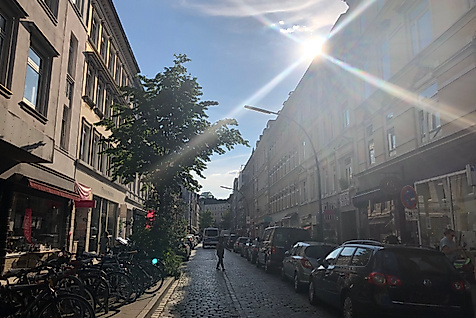 Sonnenlicht fällt auf die lebendige Bahrenfelder Straße mit kleinen Läden, Cafés und geparkten Fahrrädern