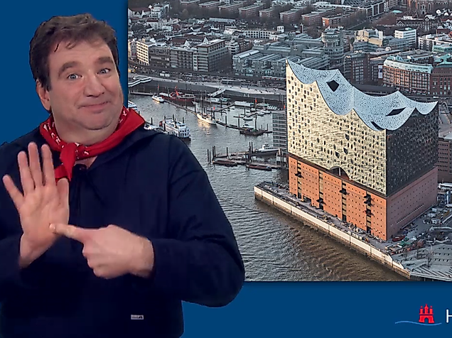 Man signing in International Sign in front of the Elbphilharmonie and Hamburg’s HafenCity.