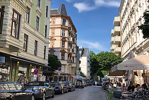 Lebendige Schanzenstraße in Hamburg mit Altbauten, kleinen Läden, Cafés und Passant:innen bei Sonnenschein