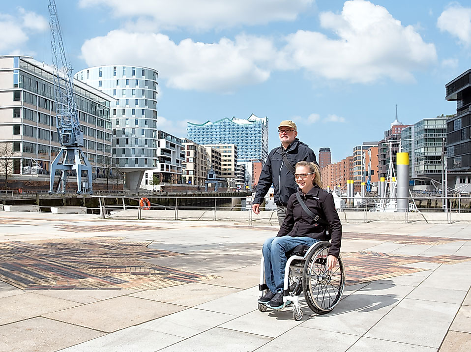 Rollstuhlfahrerin mit Begleitperson auf barrierefreier Tour durch die moderne Hamburger HafenCity.