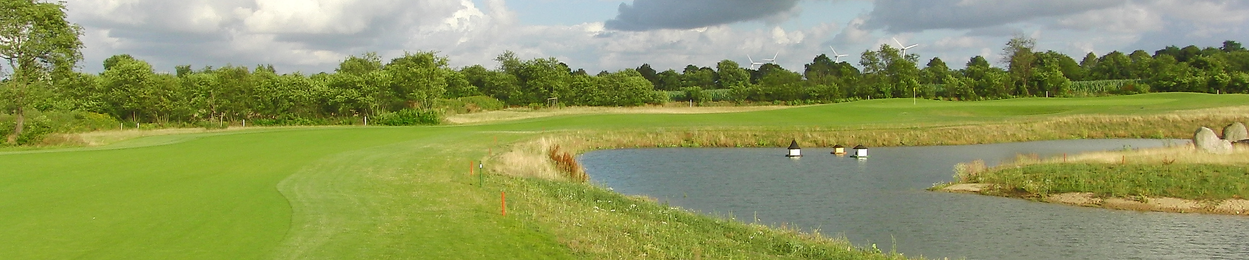 Spielbahn mit Wasserhindernis auf dem Golfplatz Golf am Donner Kleve bei Hamburg unter wolkigem Himmel