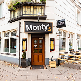 Außenansicht des Restaurants Monty’s in Hamburg mit Holztür, heller Fassade und Außengastronomie auf dem Gehweg