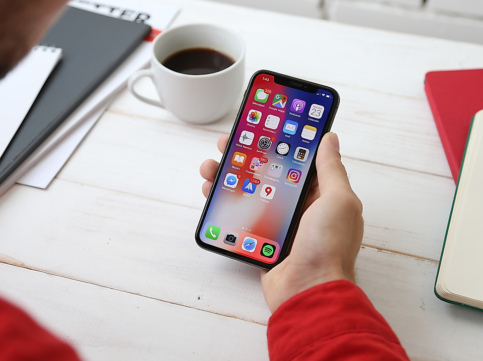 Person am Schreibtisch nutzt Smartphone mit geöffneter App-Übersicht, Symbol für digitales Marketing