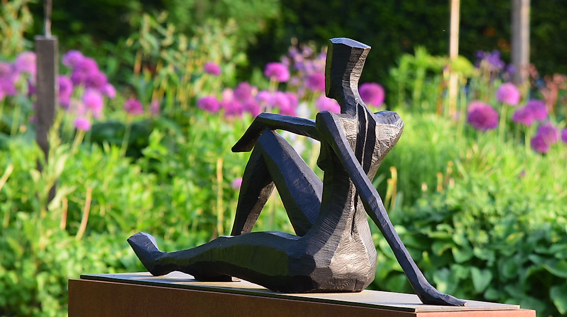 Bronzene weibliche Skulptur vor blühenden Pflanzen