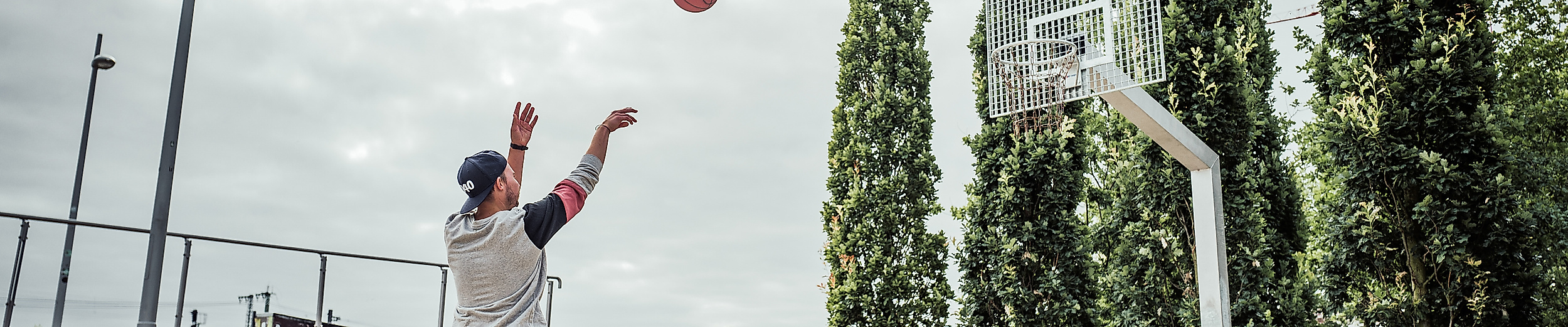 Person wirft Basketball auf dem Spielfeld im Lohsepark, umgeben von Bäumen und moderner Parkanlage
