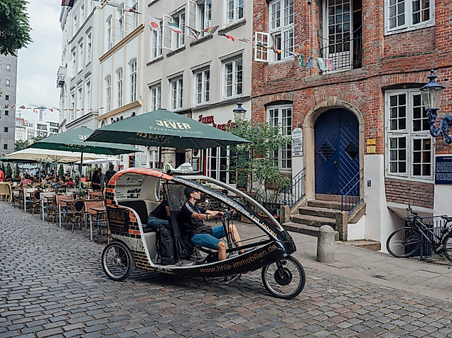 Rikscha fährt durch enge Altstadtgasse mit Außengastronomie und historischen Fassaden in Hamburg