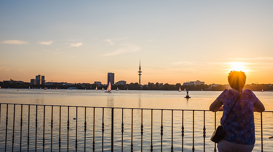 Person blickt im Abendlicht über die Außenalster, im Hintergrund Skyline und Segelboote
