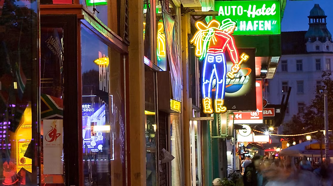 Leuchtende Neonreklamen und Schilder auf der Reeperbahn in Hamburg bei Abenddämmerung mit belebter Straße