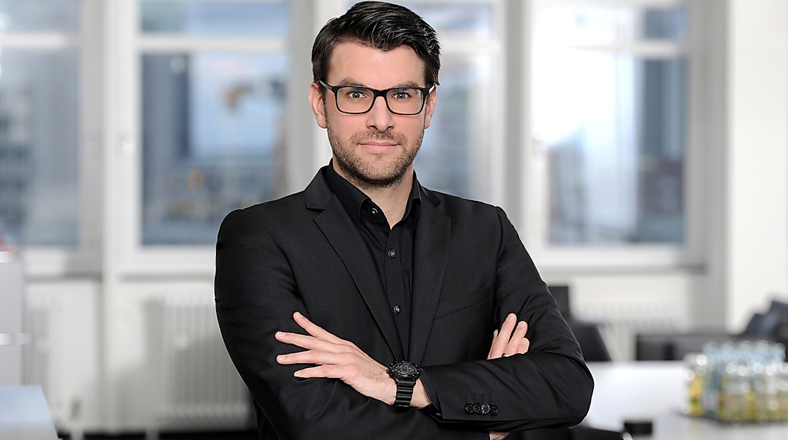 Porträt eines Mannes mit Brille im schwarzen Anzug vor hellem Konferenzraum, Ansprechpartner der Hamburg Tourismus GmbH