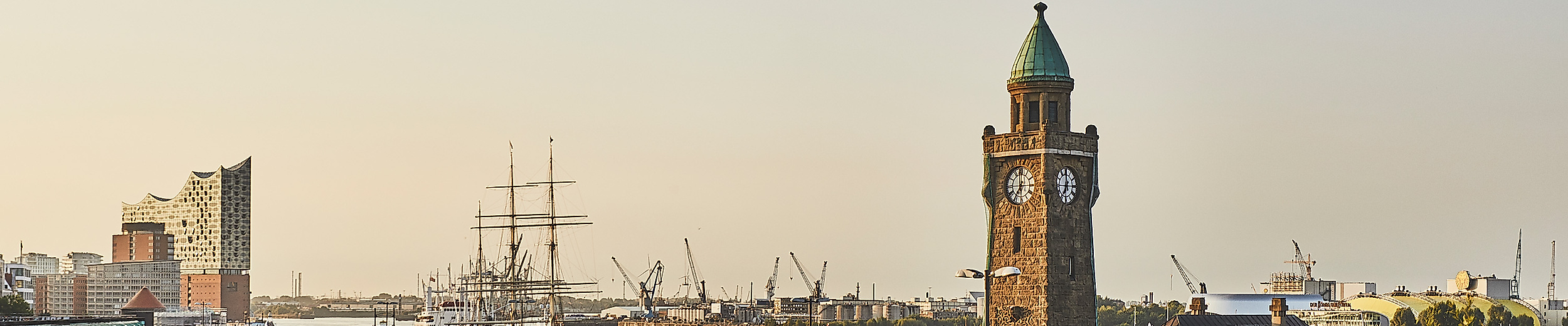 Sonnenaufgang über den Landungsbrücken mit Uhrturm, Elbphilharmonie und ruhiger Elbe im Morgenlicht