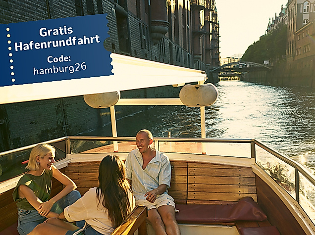 Drei Personen auf einer Barkasse bei Sonnenuntergang, Speicherstadt im Hintergrund, Hinweis auf "Gratis Hafenrundfahrt mit Code: hamburg2026"