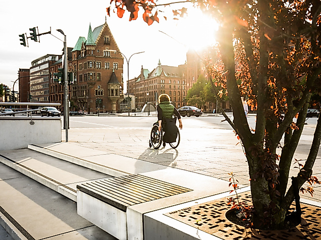 Person im Rollstuhl auf barrierefreiem Weg in der Hamburger Speicherstadt bei Sonnenlicht.