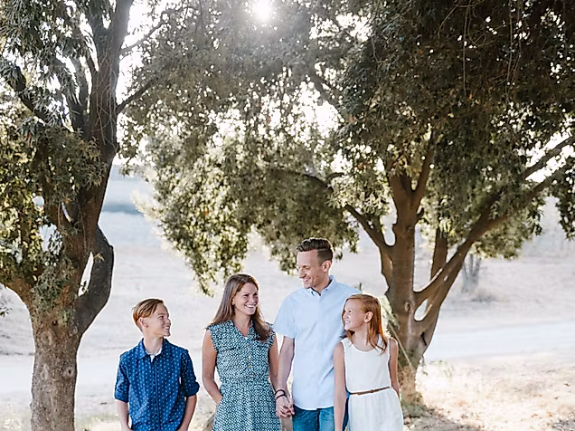 Familie mit zwei Kindern spaziert entspannt durch eine sonnige Baumallee – gemeinsame Zeit im Grünen