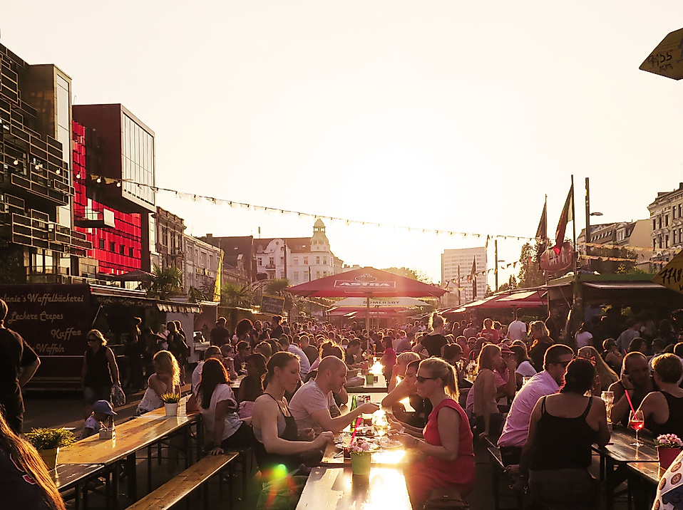 Zahlreiche Menschen genießen den Sonnenuntergang auf dem belebten Spielbudenplatz mit Gastronomie und Lichterketten