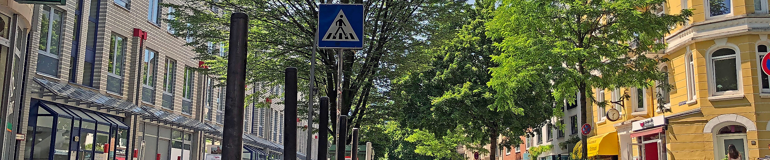 Grüne Bäume säumen die Gertigstraße in Hamburg, umgeben von Altbauten, Cafés und kleinen Geschäften