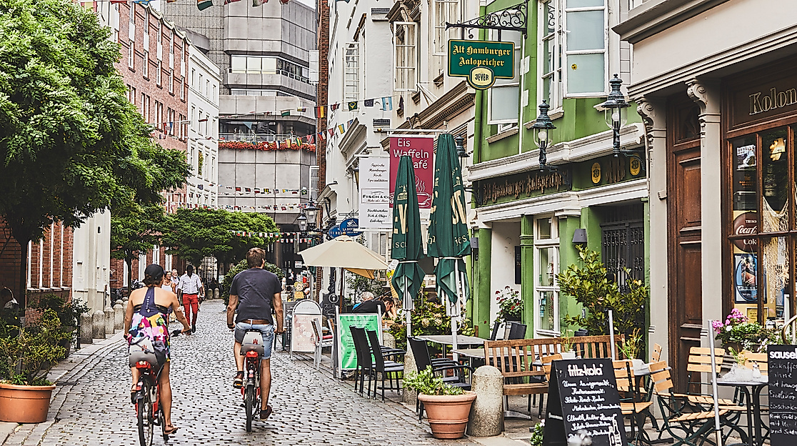 Belebte Deichstraße mit historischen Fassaden, Außengastronomie und Passant:innen bei Tageslicht