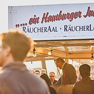 Verkaufsstand „ein Hamburger Jung“ mit Besucher:innen auf dem Fischmarkt bei Sonnenaufgang