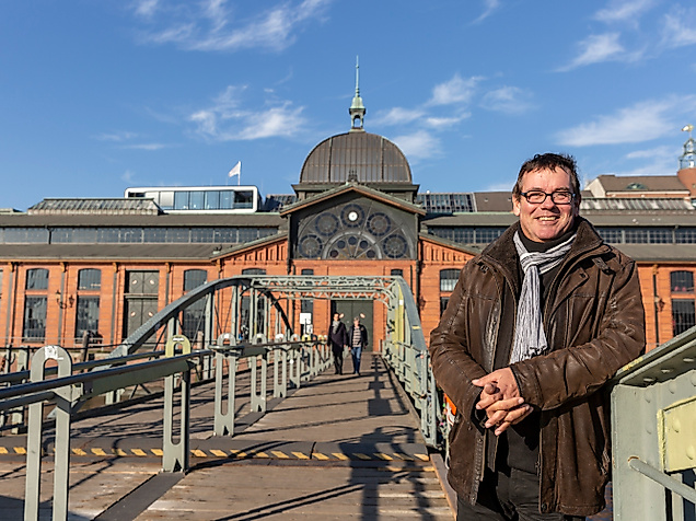 Person auf Brücke vor der Hamburger Fischauktionshalle bei Sonnenschein und blauem Himmel