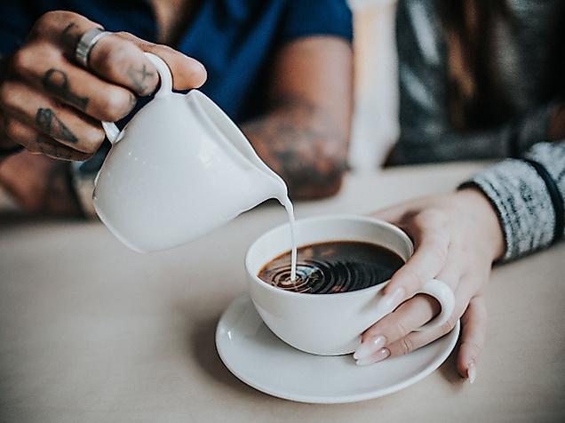 Eine Hand gießt Milch in eine Tasse Kaffee, die von einer anderen Person gehalten wird