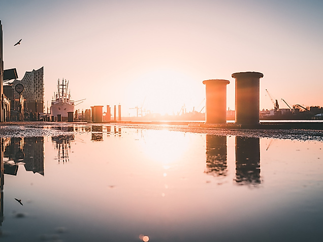 Sonnenaufgang im Hamburger Hafen mit Spiegelung auf nasser Kaimauer und Silhouetten von Kränen und Gebäuden