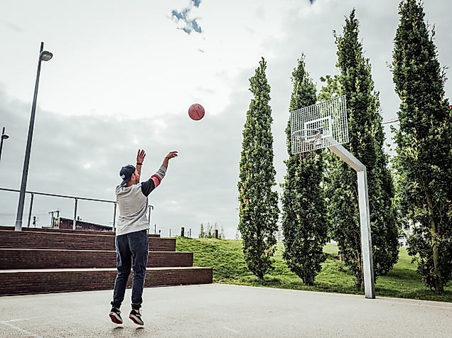 Person wirft Basketball auf dem Spielfeld im Lohsepark, umgeben von Bäumen und moderner Parkanlage