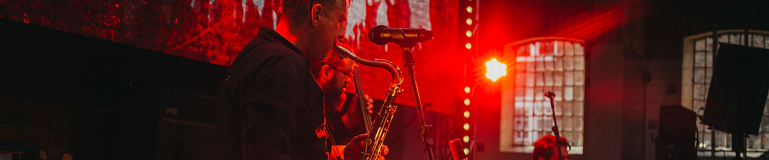 Livemusik in rotem Licht: Saxofonist spielt auf kleiner Bühne in stimmungsvoller Bar-Atmosphäre