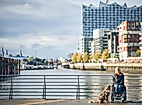 Rollstuhlfahrerin mit Assistenzhund in der HafenCity Hamburg, im Hintergrund Elbphilharmonie