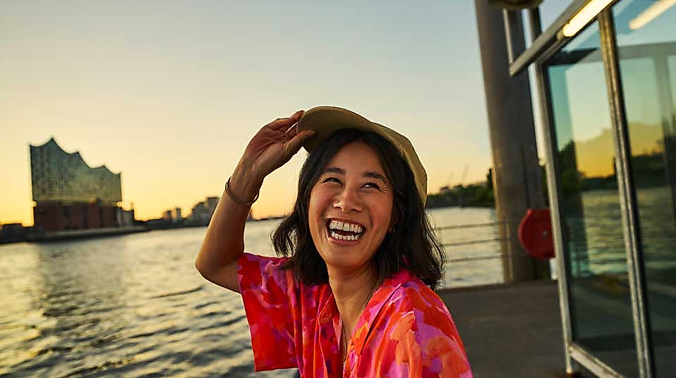 Touristin mit Hamburg CARD genießt Sonnenuntergang am Hafen mit Blick auf die Elbphilharmonie.