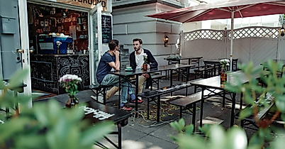 Zwei Personen sitzen im Außenbereich von Playground Coffee, umgeben von Pflanzen und roten Sonnenschirmen