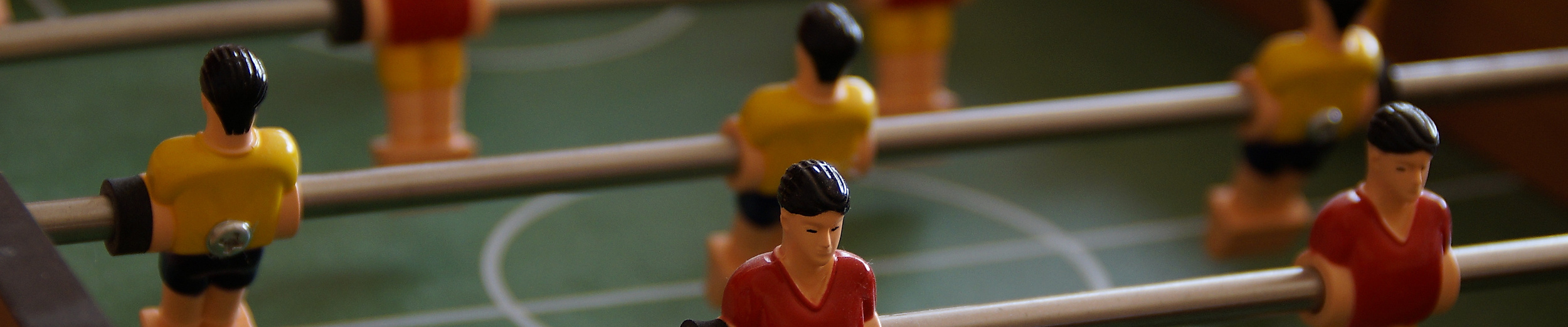 Nahaufnahme eines Tischkickers mit rot-gelben Spielfiguren auf grünem Spielfeld