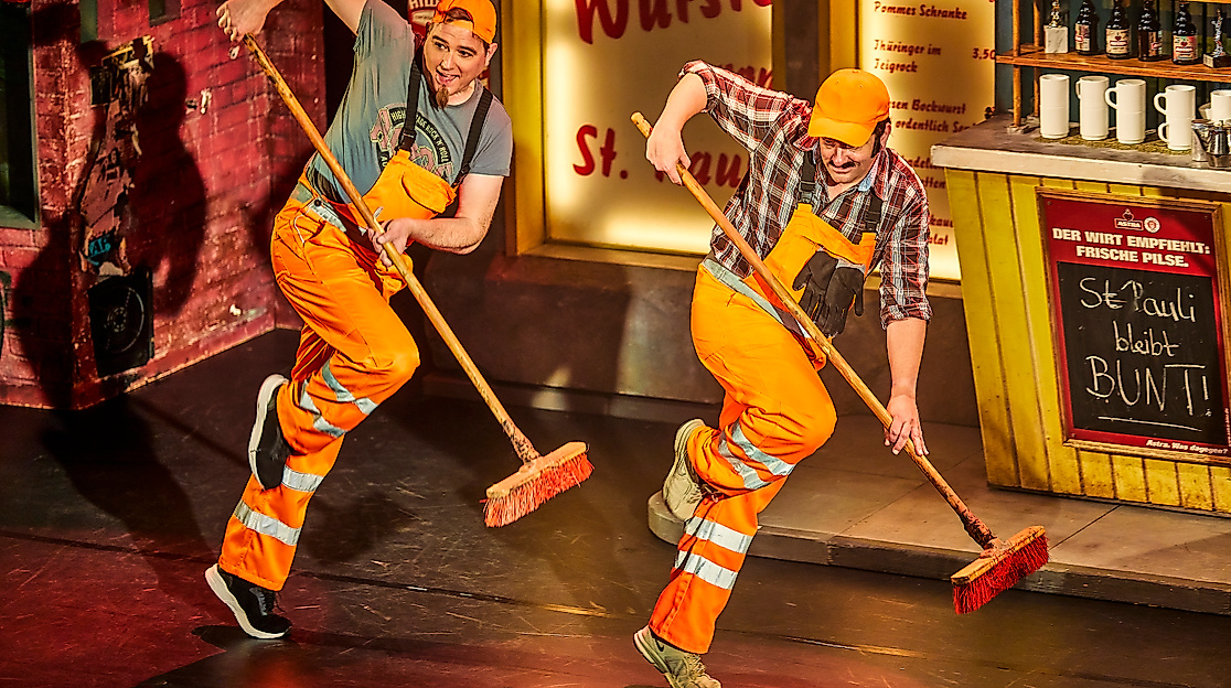 Szenenbild Heiße Ecke: 2 Menschen machen choreographisch die Bühne sauber