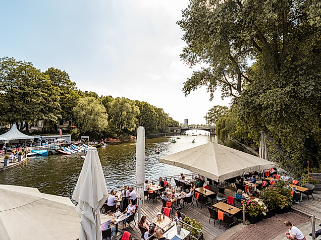 Gut besuchter Biergarten am Wasser mit Sonnenschirmen und Blick auf den Alsterlauf beim Anleger 1870
