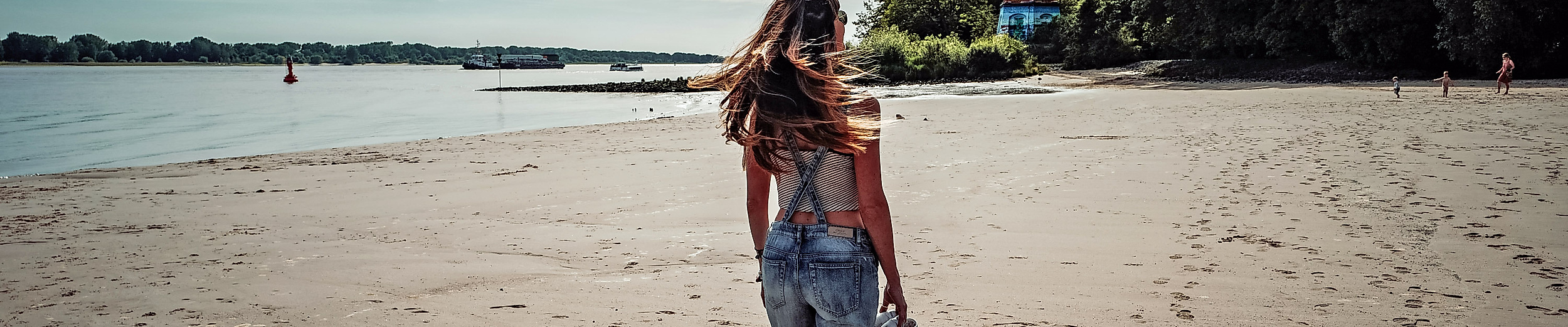 Frau trägt Kind am Elbstrand Wittenbergen, barfuß im Sand mit Leuchtturm im Hintergrund