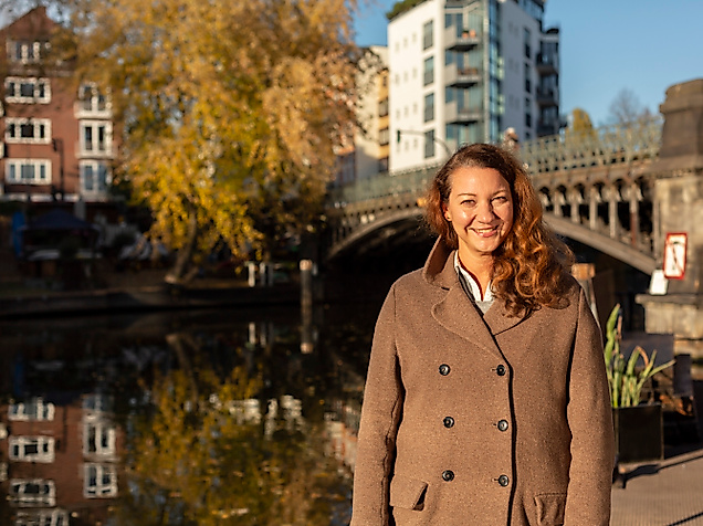 Lächelnde Frau vor Brücke und Kanalufer an der Hamburger Alster bei Sonnenlicht und herbstlicher Stimmung