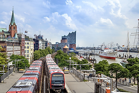 U-Bahn fährt an den St. Pauli Landungsbrücken entlang, im Hintergrund Elbphilharmonie und Museumsschiffe.