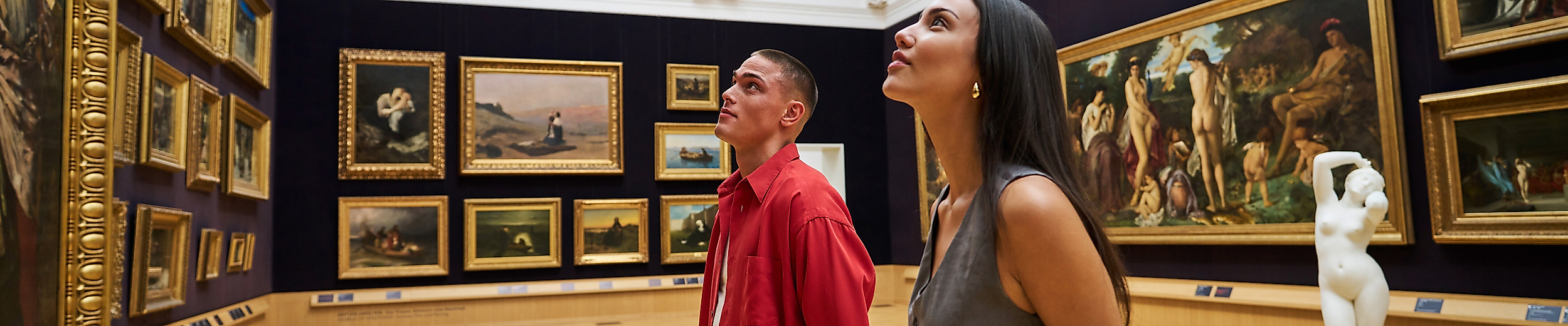 [Translate to English:] Zwei junge Erwachsene betrachten Bilder in einem historischen Saal der Kunsthalle Hamburg.