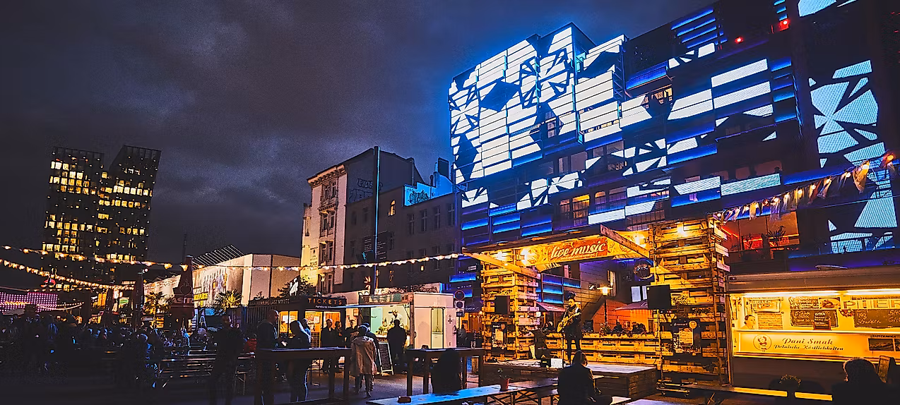 Spielbudenplatz bei Nacht mit beleuchteten Fassaden, Food-Ständen und leuchtender Straßenkunst in Blau und Gelb