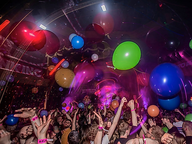 Bunte Party mit Luftballons, Lichteffekten und jubelndem Publikum in ausgelassener Queer-Bar-Atmosphäre