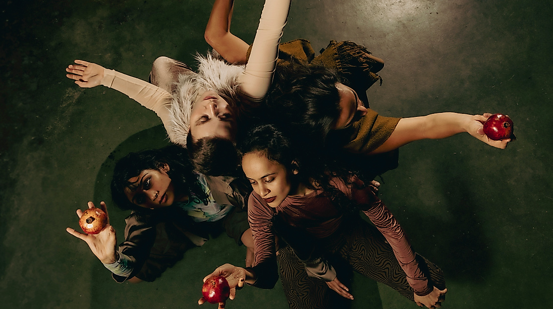 Eine Gruppe Menschen sind eng umschlungen im Kreis. In den Händen halten sie eine Frucht.