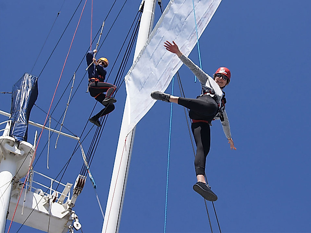 Zwei gesicherte Personen klettern im Hochseilgarten auf der Cap San Diego vor blauem Himmel