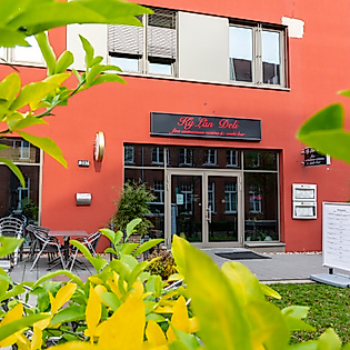 Eingang eines Restaurants in Hamburg mit moderner roter Fassade und Begrünung im Vordergrund